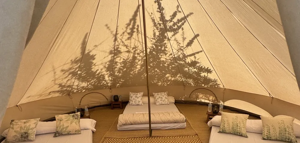 Interior d'un tipi amb llit fet, roba de llit clara i la llum del capvespre a través de la lona
