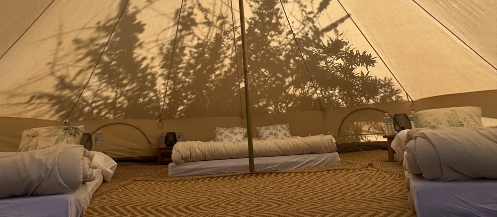 Interior d'un tipi amb matalassos preparats i les ombres de les plantes sobre la lona